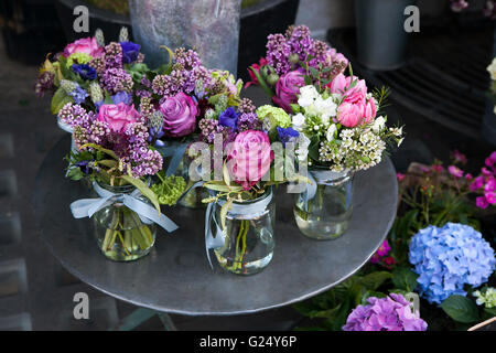 Kleine Sträuße aus Flieder, Hyazinthen, Anemonen, Rosen und Pfingstrosen in kleinen Gläsern auf ein Eisentisch. Stockfoto