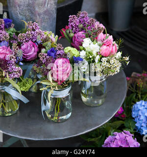 Kleine Sträuße aus Flieder, Hyazinthen, Anemonen, Rosen und Pfingstrosen in kleinen Gläsern auf ein Eisentisch. Stockfoto