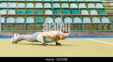 Junge sportliche Frau Kern Übung im Stadion. Lächelnde kaukasische Mädchen tun drängen sich auf dem Rasen Stockfoto