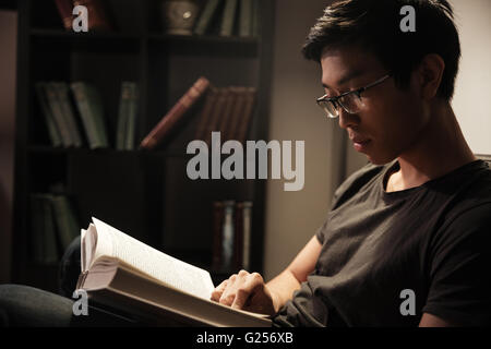 Attraktive ruhige Jüngling in Gläsern sitzen und lesen Buch zu Hause Stockfoto
