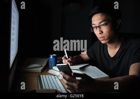 Hübschen asiatischen jungen Mann mit Smartphone während seines Studiums am Abend zu Hause Stockfoto