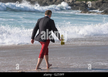 Ein elegant gekleideter Mann nimmt ein Abend Fistral Strand in Newquay, Cornwall entlang schlendert. Stockfoto