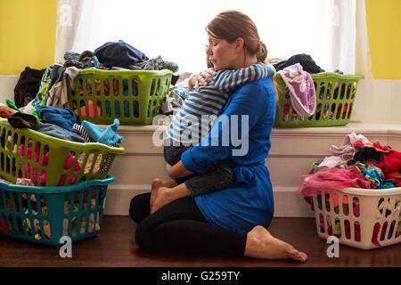 Mutter umarmt Sohn, umgeben von Wäschekörbe Stockfoto