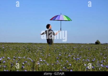 Mann steht im Feld mit einem bunten Regenschirm Stockfoto