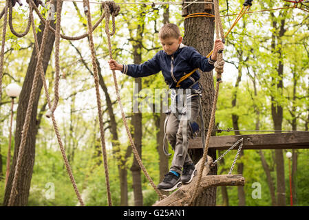 Junge in Seilgeschirr auf Klettern Plattform im Baum im Abenteuerpark Stockfoto