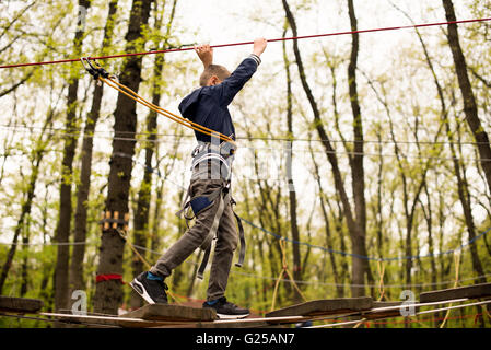 Junge in Seilgeschirr auf Klettern Plattform im Baum im Abenteuerpark Stockfoto