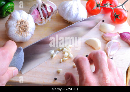Chef hacken Knoblauch auf einem Schneidetisch auf ein Schneidebrett in der Küche Draufsicht gekocht werden Stockfoto