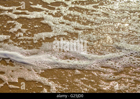 Seafoam am Sandstrand Stockfoto