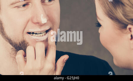 Hygiene und Pflege-Konzept. Junge blonde weibliche Kosmetikerin Kosmetikerin Creme auf männliche Mund Lippen auftragen. Frau und Mann mit Kosmetik zu spielen. Stockfoto