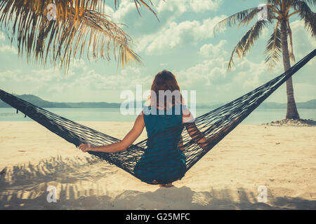 Jahrgang gefiltert Aufnahme einer jungen Frau sitzt in einer Hängematte an einem tropischen Strand Stockfoto