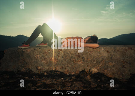 Eine junge Frau liegt auf einem ungewöhnlichen Felsen bei Sonnenaufgang Stockfoto