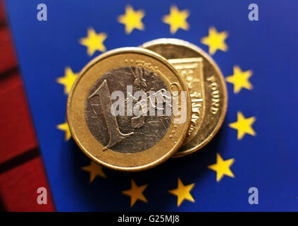 Eine 1-Euro-Münze und eine demjenigen Pfund-Münze auf dem Hintergrund der europäischen Flagge in London. Stockfoto