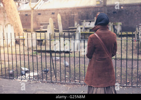 Eine Frau füttert einige Tauben auf einem Friedhof Stockfoto