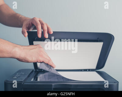 Die Hände eines jungen Mannes setzt ein Stück Papier auf einen Flachbett-Scanner in Vorbereitung auf Kopieren Stockfoto