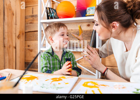 Niedlichen kleinen Jungen und seiner Mutter sitzen und Spaß mit ihren bemalten Händen in bunten Farben Stockfoto