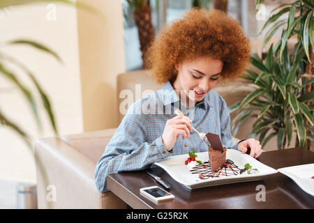 Niedliche lockige junge Frau mit roten Haaren Essen Dessert im café