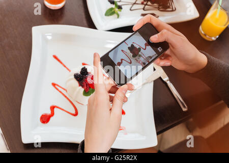 Draufsicht der jungen Frau die Hände Fotografieren von leckere Süßspeise auf weißen quadratischen Platte mit smartphone Stockfoto