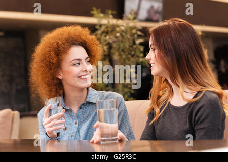 Zwei glückliche attraktive junge Frauen Lächeln und Trinkwasser im café Stockfoto