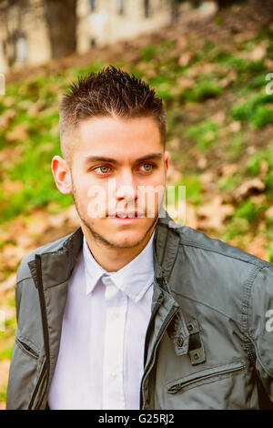 Schönen jungen Mann sitzt auf der Bank im Park im Herbst mit Laub rund um Stockfoto