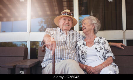 Porträt von schöner senior Mann sitzt mit seiner Frau auf einer Bank vor ihrem Haus. Rentner Ehepaar eine Pause und entspannen
