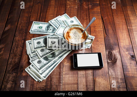 Kaffeetasse, Geld, Dollar und Telefon auf Vintage Holztisch Hintergrund. Stockfoto