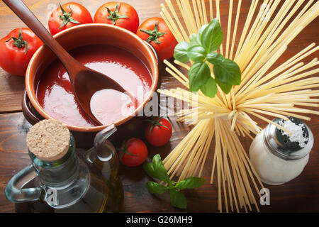 Tomatensauce auf einem Terrakotta-Topf mit Zutaten und Spaghetti Nudeln von oben gesehen. Stockfoto