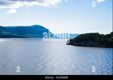 Ozean Einlass unter bewaldete grüne Berge und Küste unter blauem Himmel mit Wolken, in Neufundland, Kanada. Stockfoto