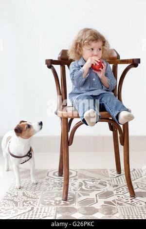 Kleines Kind ißt Apfel in Studio und Hund auf der Suche Stockfoto