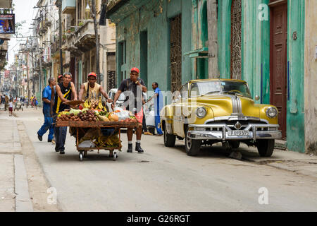 Obst und Gemüse Verkäufer schiebt ihren Wagen vorbei an zwei amerikanischen Oldtimern (Pontiac) in Havanna, Kuba Stockfoto