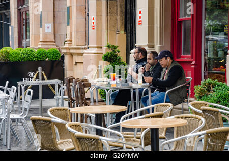 Drei Männer sitzen vor einem Café mit Getränken. Stockfoto