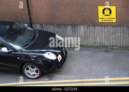 Illegales parken, schwarzen Auto parkte auf doppelte gelbe Linien neben ein Warnhinweis über Rad spannen. 24. Mai 2016 Stockfoto