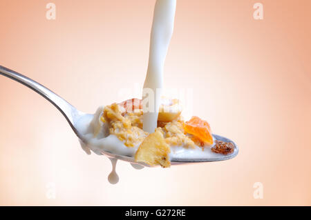 Milch auf einen Löffel voll von Getreide auf Früchten und Nüssen mit isolierten Hintergrund fallen Stockfoto