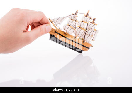 Hand in Kontakt mit einem kleinen Modell-Segelboot auf weißem Hintergrund Stockfoto