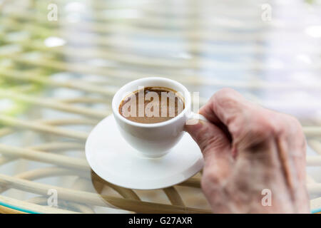Senior Türkin Hand hält eine Tasse türkischen Kaffee auf einem Glastisch Stockfoto
