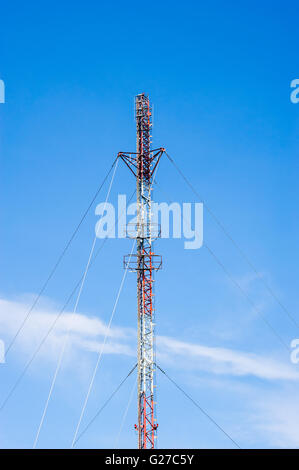 Hoch rot und weiß Metall communications Antennenmast mit mehreren Tragseile, gegen den blauen Himmel. Stockfoto