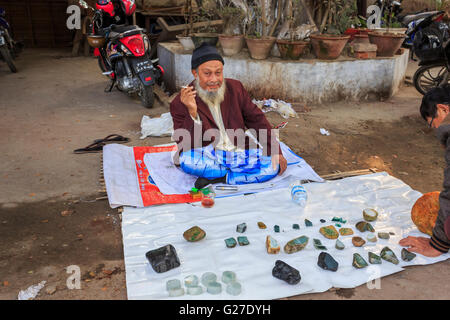 Bärtige Verkäufer mit Anzeige der Rohschnitt Stücke aus Jade auf Verkauf am Straßenrand auf dem Jademarkt, Mandalay, Myanmar (Burma) Stockfoto