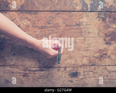 Eine weibliche Hand ist auf einem Schreibtisch aus Holz mit einem Stift schreiben. Stockfoto