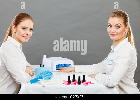 Maniküre Verfahrenskonzept. Junge Kosmetikerin und Frau Kunde im Beauty-Salon. Weiblichen Kunden hält Hände auf Deskop mit Nagellacken Handtuch Datei Beleuchtung Instrumente. Stockfoto