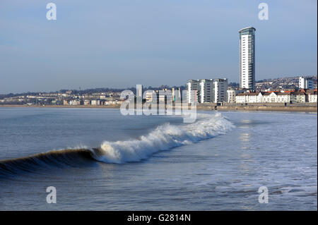 Wellen brechen an den Strand am Swansea Meer nah an dem Aufstellungsort der vorgeschlagenen Gezeiten-Lagune. Swansea Turm stehen am Horizont Stockfoto