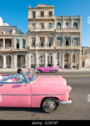 Ein 1952 rosa Ford Cabrio Fahrt entlang des Malecón in Havanna, Kuba mit einem alten Gebäude im Hintergrund heruntergekommen. Stockfoto