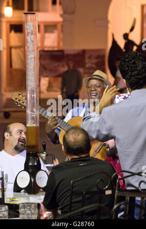 Traditionelle kubanische Musiker Gitarrist unterhält Menschen trinken in einer Bar im Freien auf der Plaza Vieja, Havanna, Kuba. Stockfoto