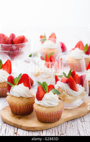 Hausgemachte Buttercreme Cupcakes mit Erdbeeren und frischer Minze und Schwamm-Torte mit Erdbeeren in ein Glas auf weißem Holz Stockfoto