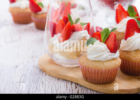 Hausgemachte Buttercreme Cupcakes mit Erdbeeren und frischer Minze und Schwamm-Torte mit Erdbeeren in ein Glas auf weißem Holz Stockfoto