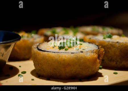 Tief gebratener Sushi garniert mit Schnittlauch serviert auf einer hölzernen Platte (Nahaufnahme). Stockfoto