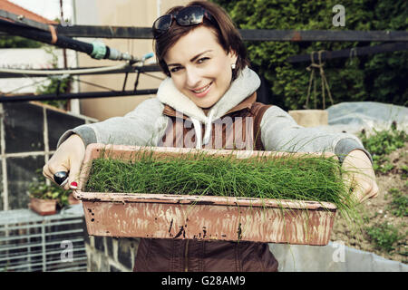 Freudige kaukasischen junge Frau mit Topf Schnittlauch im Garten. Saisonale Gartenarbeit Thema. Gärtner Frau posiert mit Anlage. Gro
