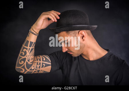 Schön und stilvoll junger Mann mit schwarzer Melone und T-shirt. Coolen Tattoos an Armen, Höhenplan Stockfoto