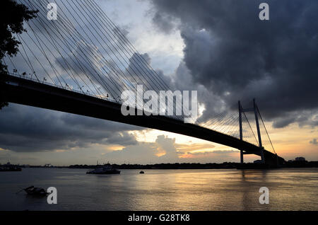 Regen Wolken schweben über zweite Hooghly Brücke bei Sonnenuntergang mit Land Angeln Boote schwimmen im Fluss unten, Kolkata, Westbengalen Stockfoto