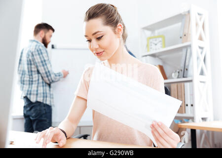 Ernste junge Geschäftsfrau mit Dokumenten arbeiten und schreiben am Computer im Büro Stockfoto