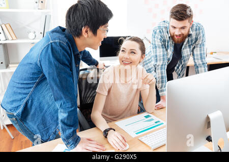 Drei fröhliche junge Geschäftsleute, die im Büro arbeiten zusammen Stockfoto