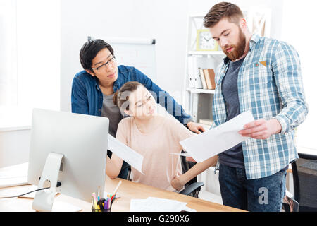 Drei konzentriert junge Unternehmer arbeiten mit Dokumenten und gemeinsamen Verwendung von Computer im Büro Stockfoto